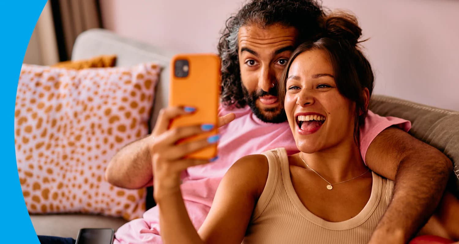 Couple laughing on the sofa while looking at a phone